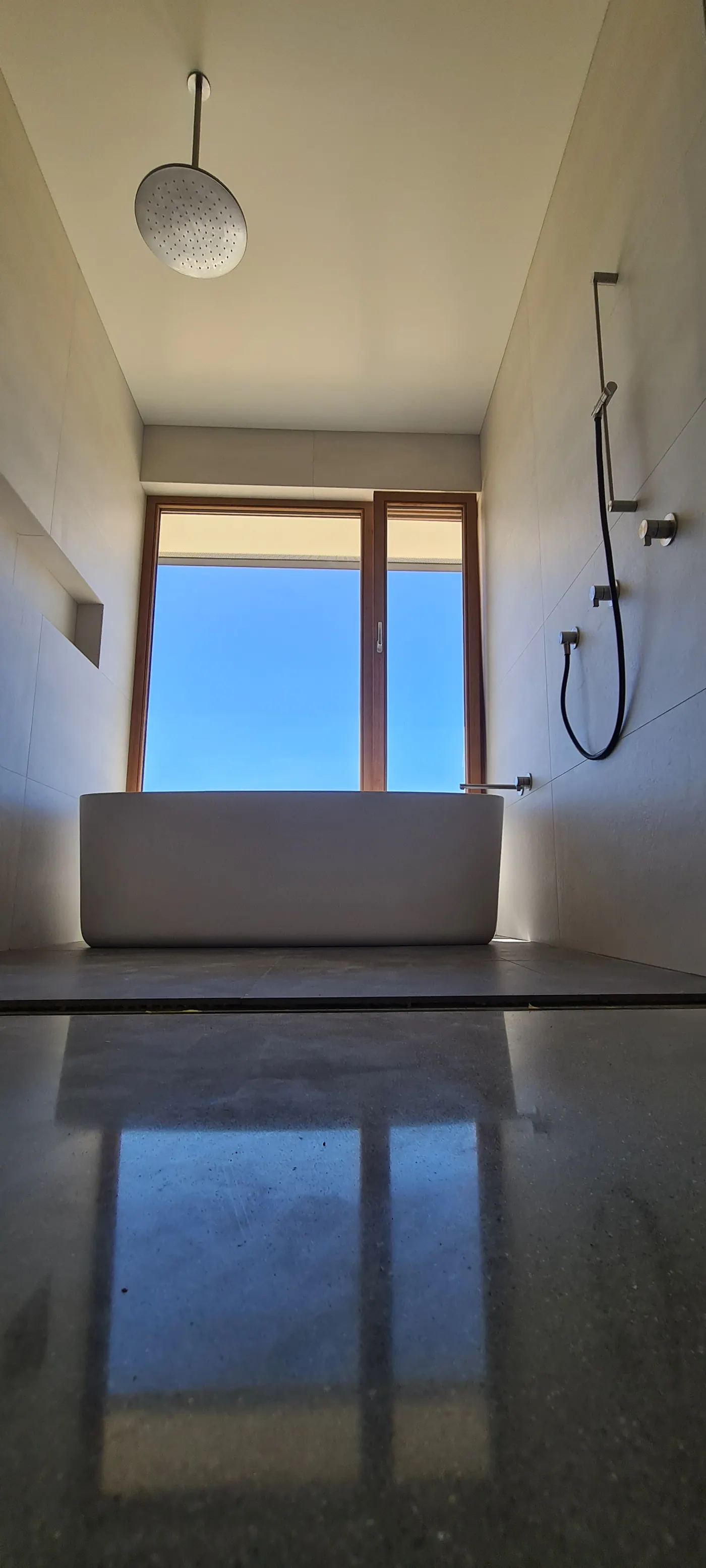 Freestanding bath and rainfall shower beneath a full-height window framing an open sky view, an Ecotectural bathroom