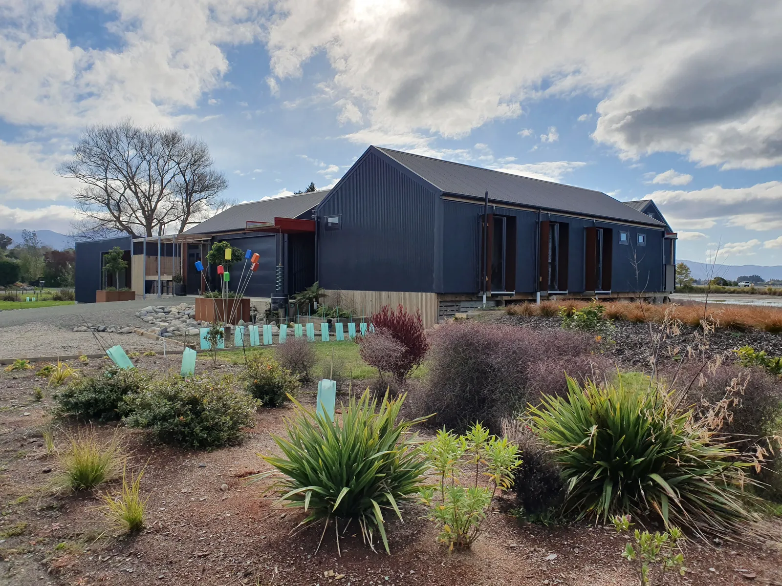The Black House, a dark board-and-batten Ecotectural home beside the Tasman estuary, with established native garden planting