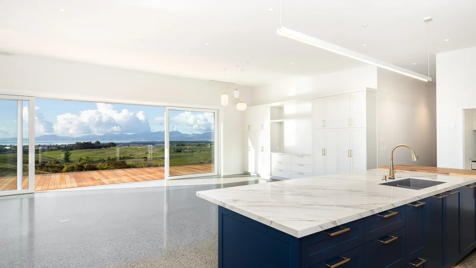 Open-plan kitchen and living with a deep blue island and sliders to the deck, looking over Tasman Bay at The Green House