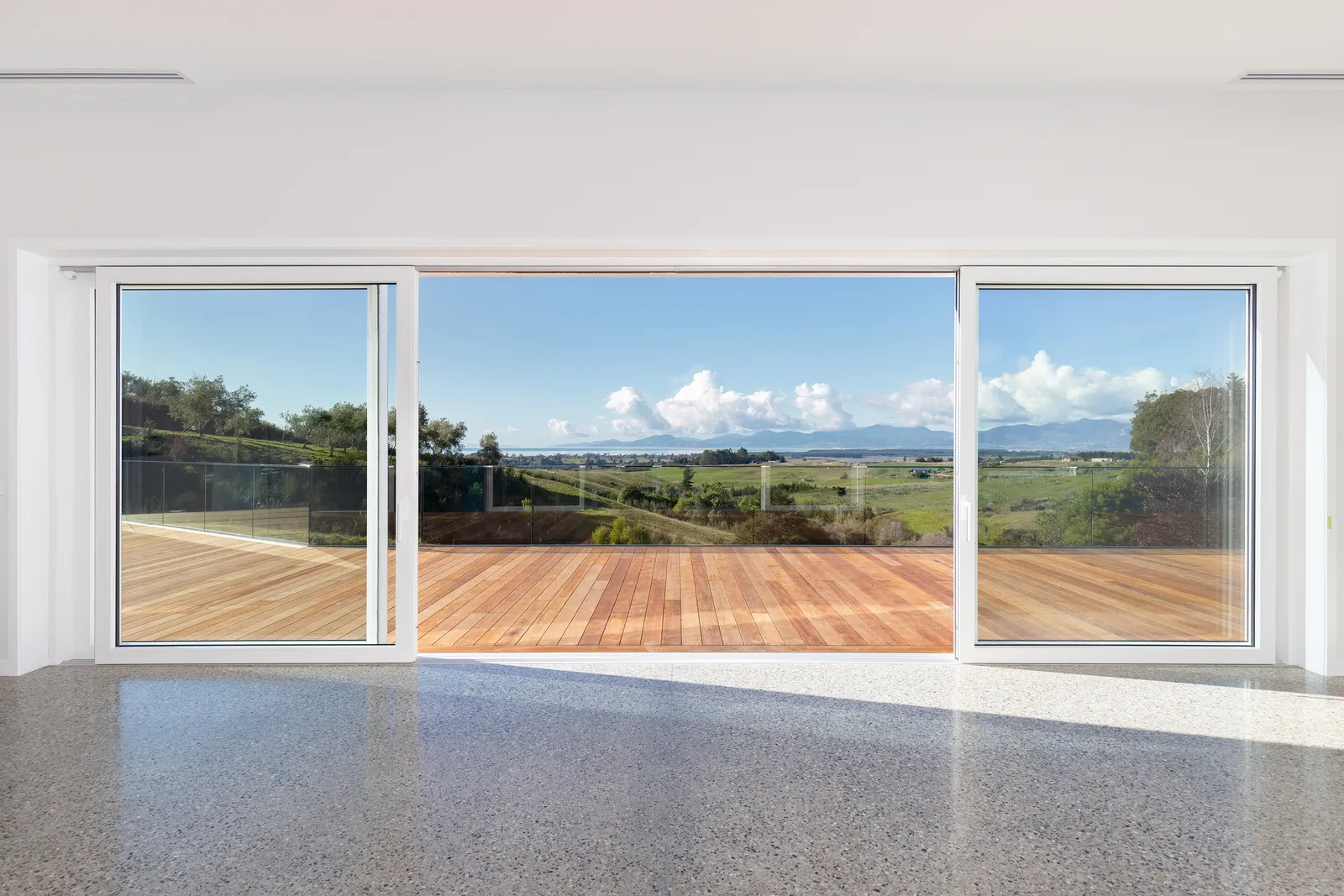 Wide estuary and mountain view through full-height sliding doors at the Blue House, an Ecotectural coastal home