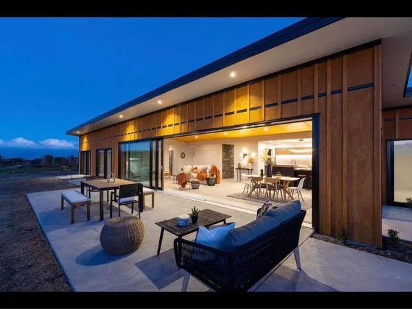 Warm-lit living room opening onto the deck at dusk, Horton Road, an Ecotectural home in Tasman