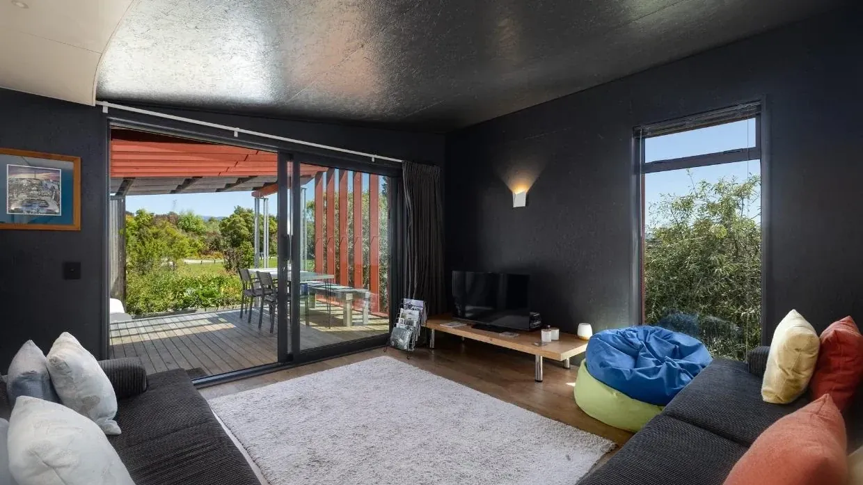 A second view of the lounge opening to the H3 pine deck at The Black House, Tasman