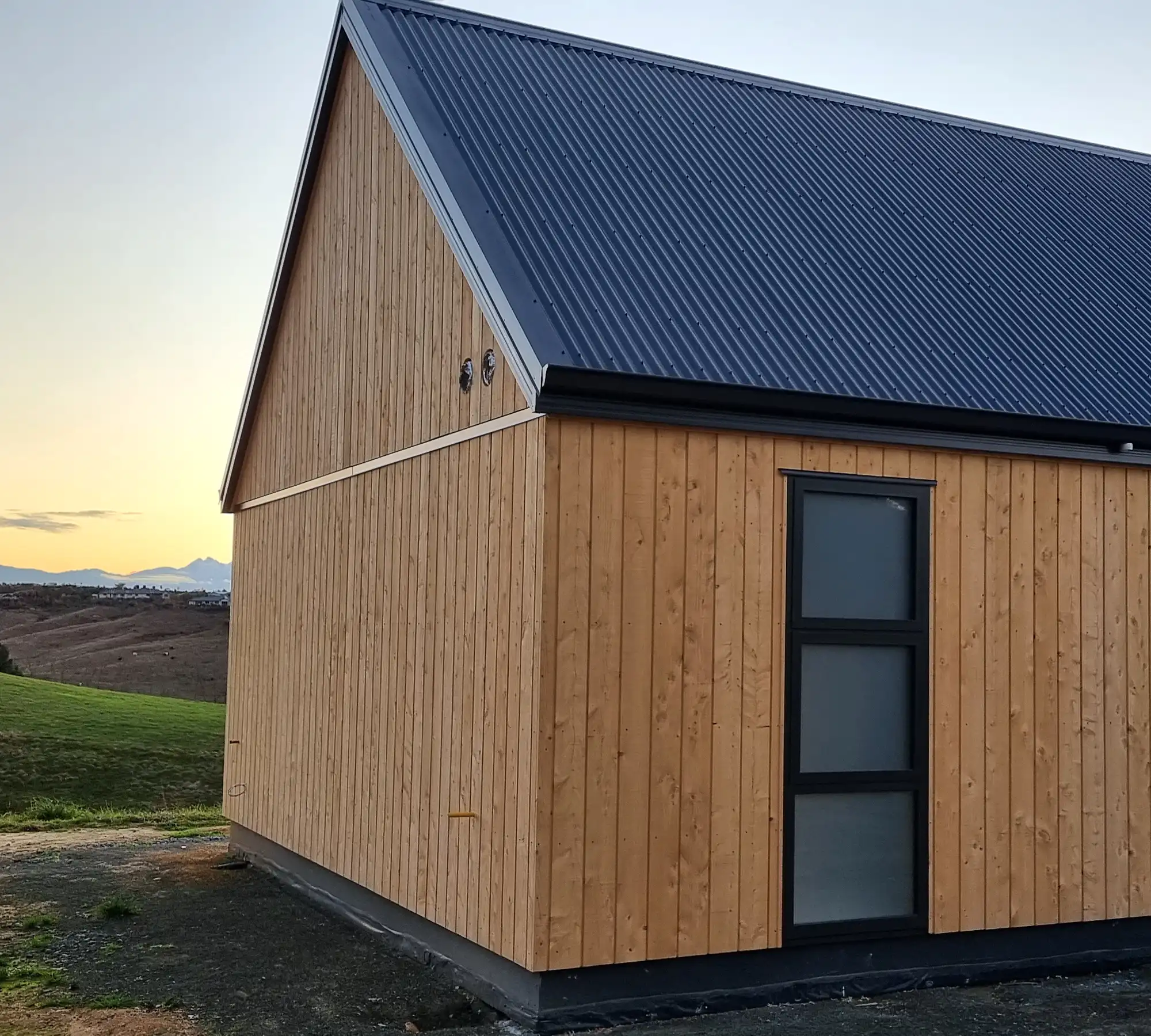 The Lawson Cypress gable end of the home at dusk, with the Waimea hills beyond, Redwood Valley