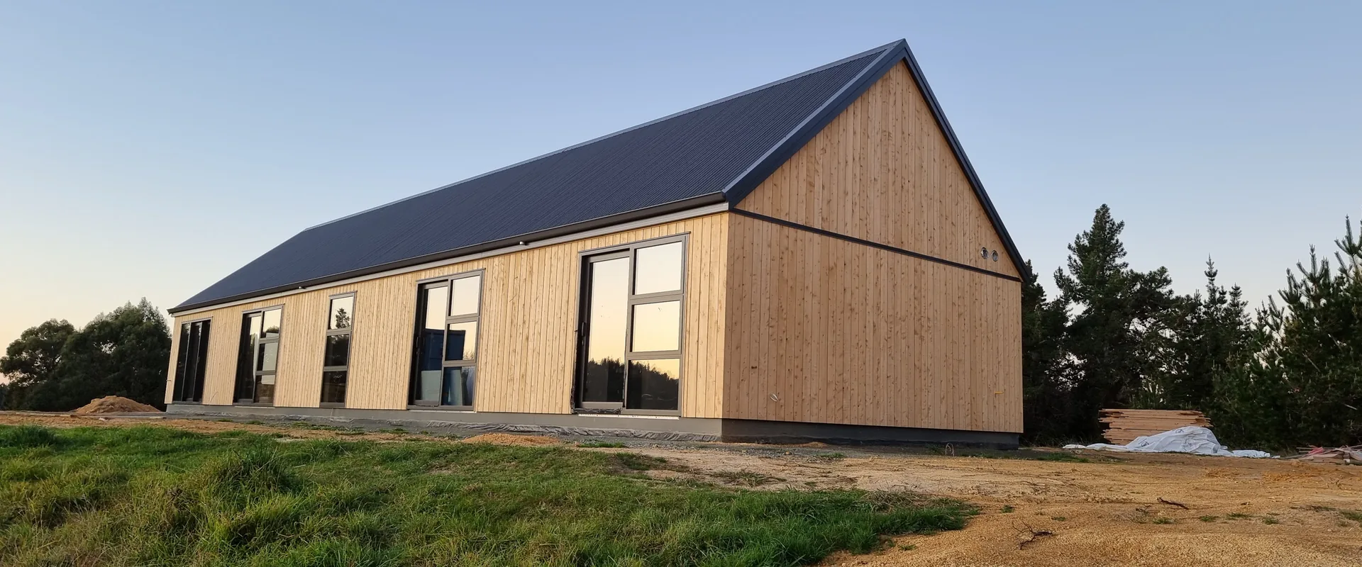 Timber-clad gable home glowing at dusk, built by Ecotectural at Redwood Valley