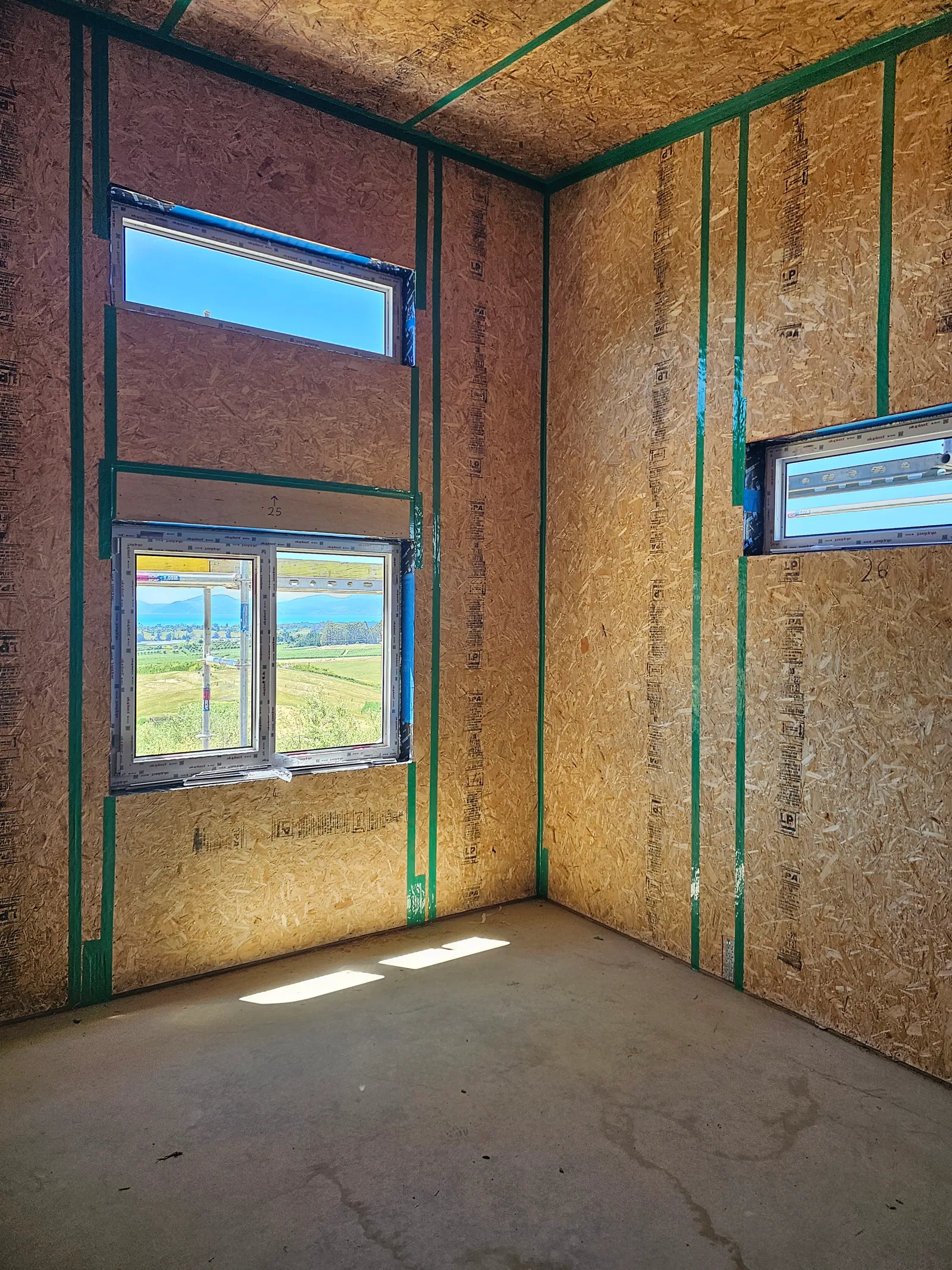 Interior of a framed room showing SIP wall panels and green airtightness tape on an Ecotectural build