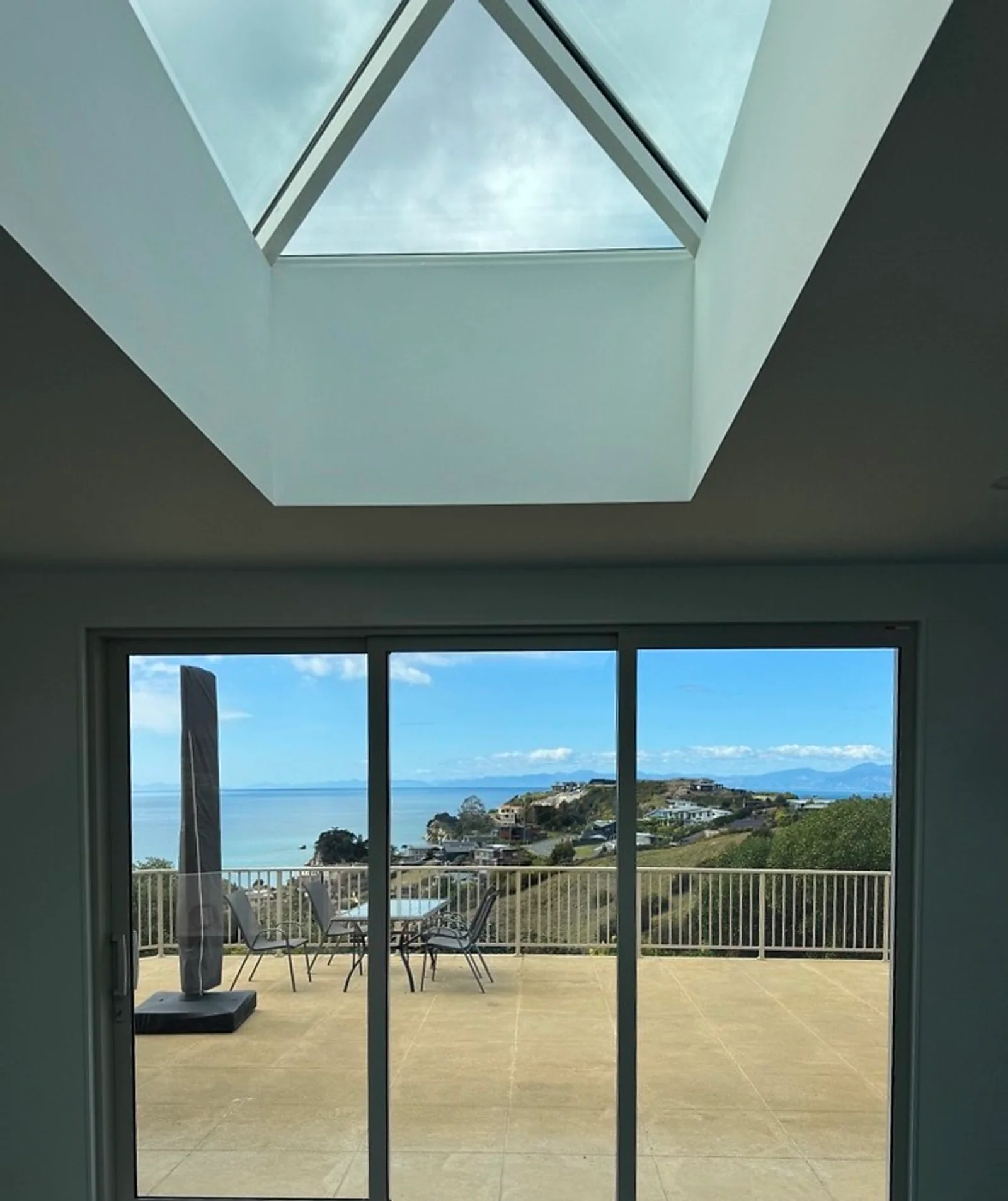 Living room skylight and sliding doors framing a coastal view over the water to the hills beyond