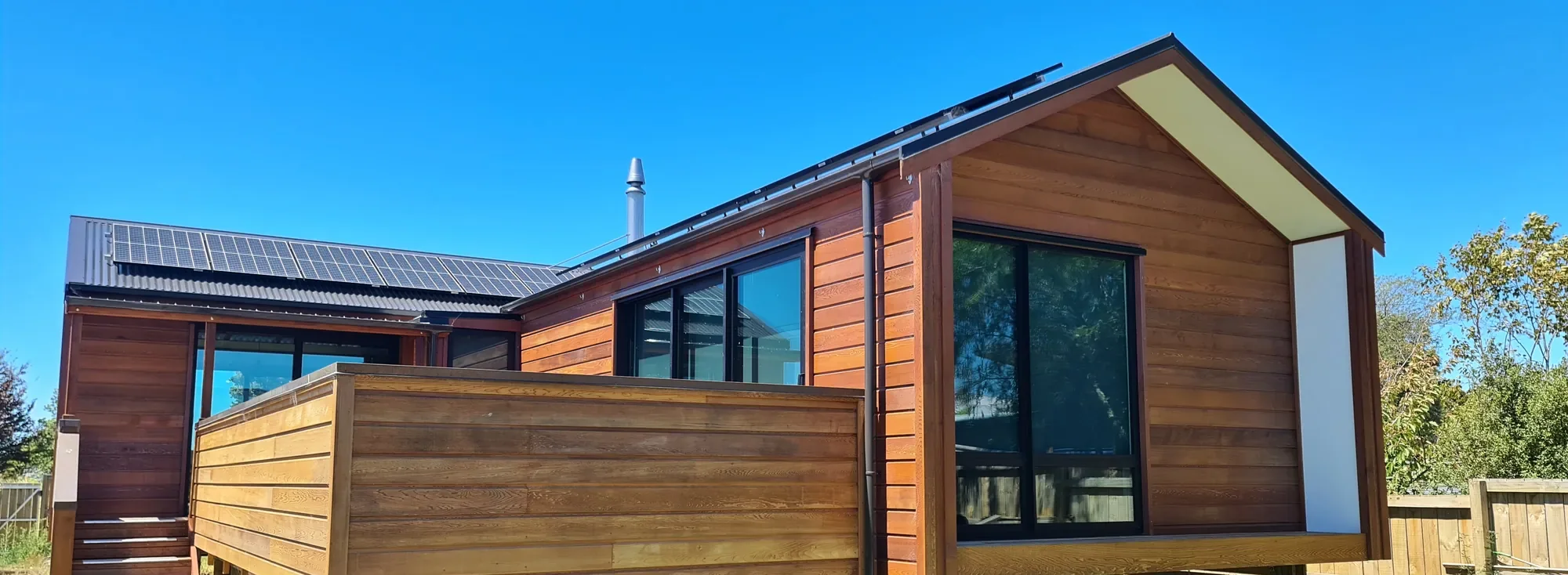 The Cedar House, a cedar-clad gable home with solar panels under a deep blue sky, Motueka