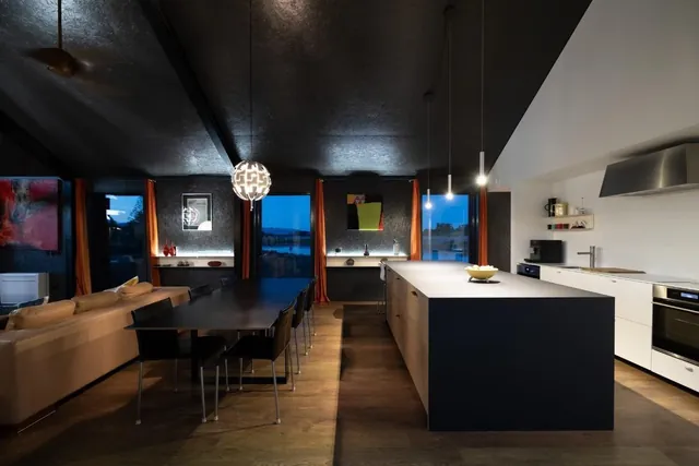 Open-plan kitchen and dining at dusk in the Black House, the About page hero