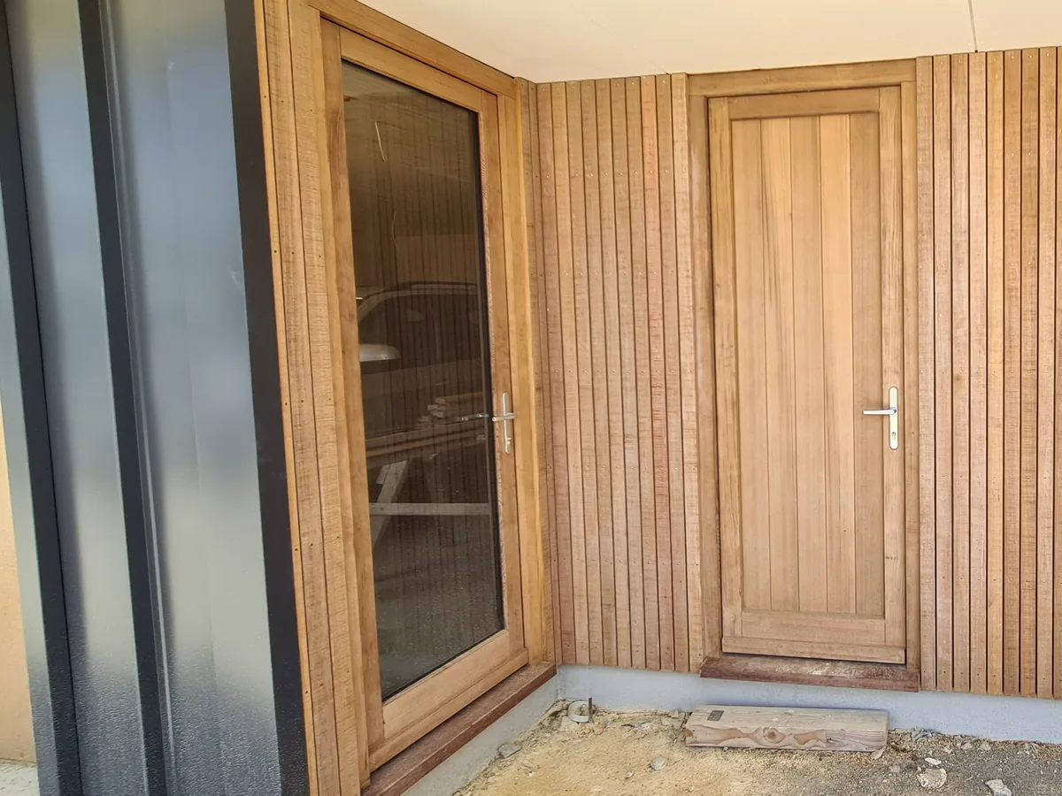 Dark steel cladding and vertical timber battens meeting at a timber entry door