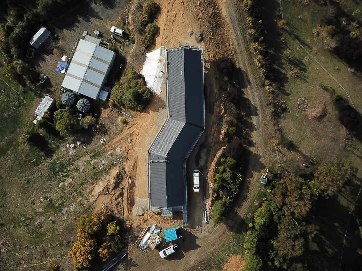 Aerial view of the long dark corrugate roof newly on over a rural Ecotectural build
