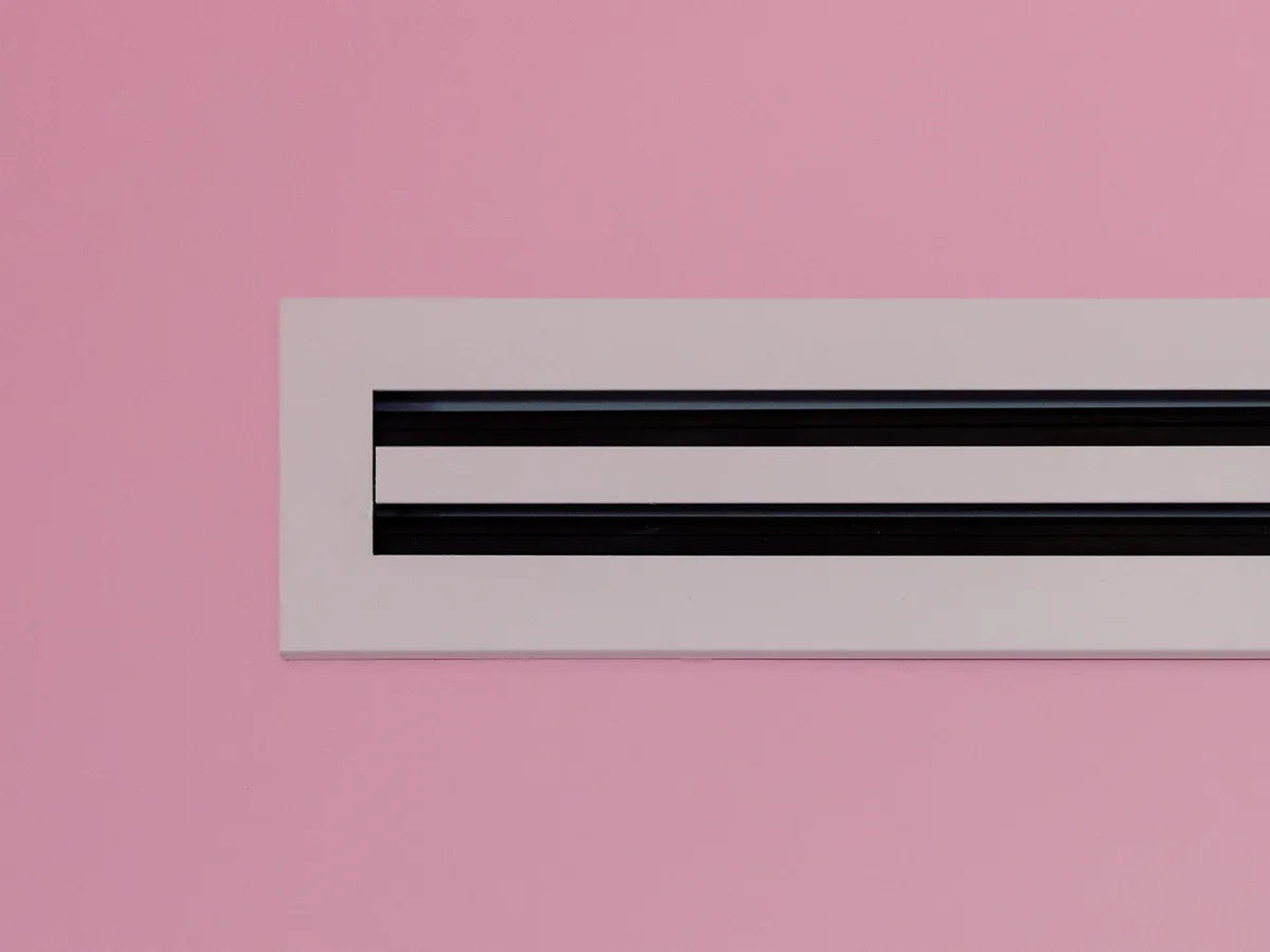 A slim linear ventilation diffuser set flush in a pink-painted wall
