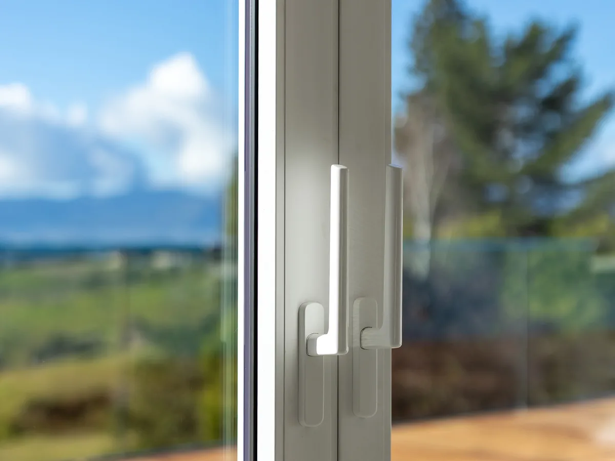 White uPVC double-glazed sliding door handles, the rural view reflected in the glass