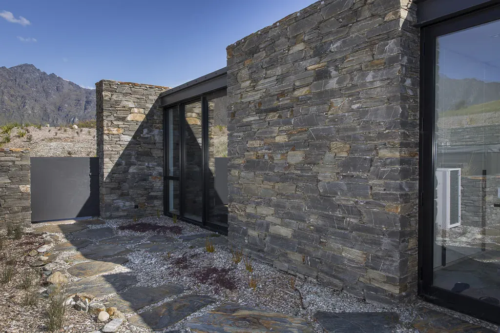 Schist stone architectural home framed by mountains, with black-framed glazing