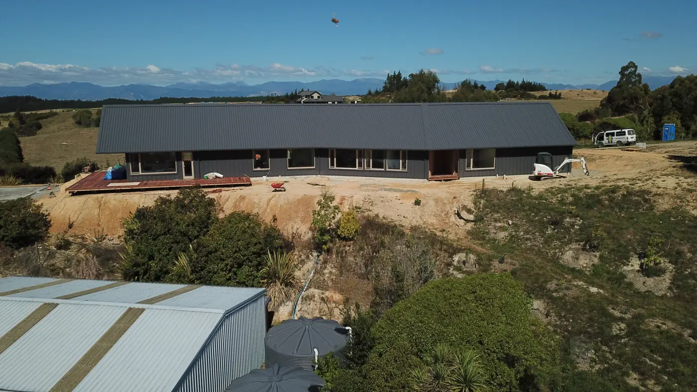 Aerial view of the long, dark-clad home on its hillside platform at Tasman View, during the build